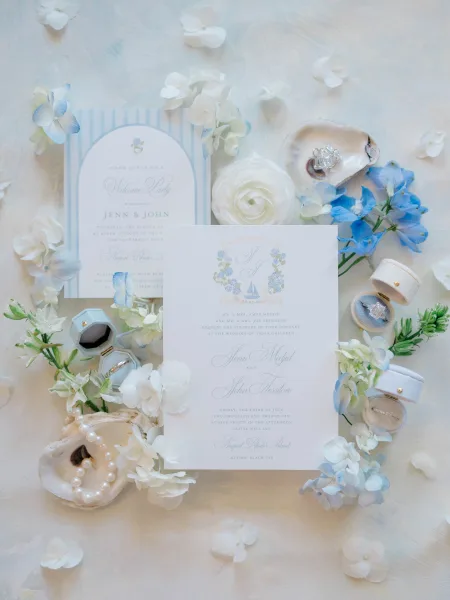 Wedding invitation suite featuring blue and white wedding invitations styled with pearls on a painted light blue backdrop
