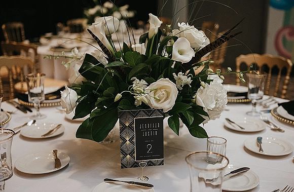 Reception tablescape with wedding table centerpiece of white calla lilies and roses, gold beaded chargers, and black napkins in reception room