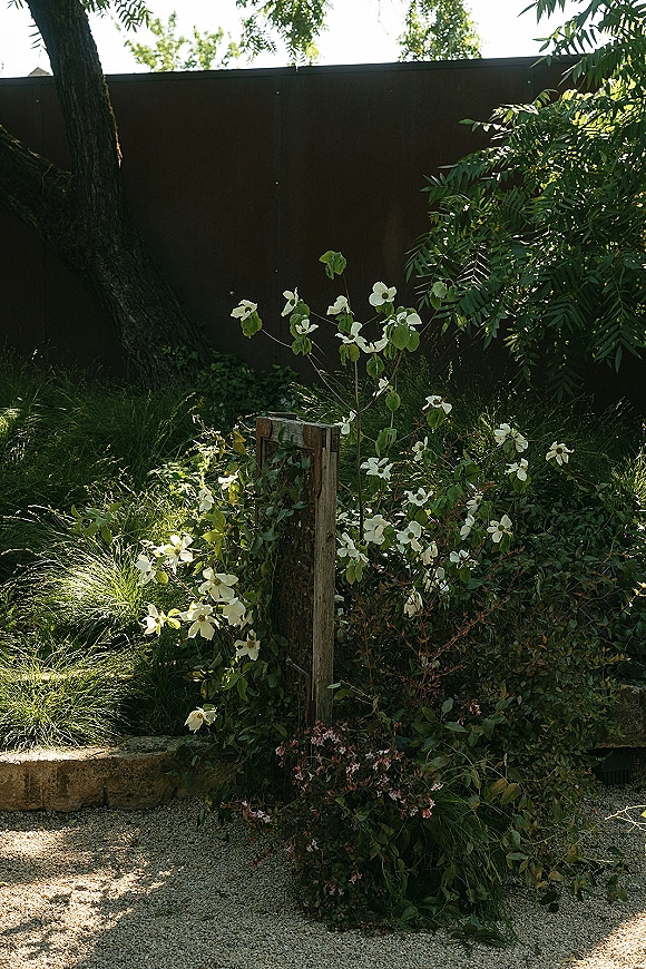Garden floral arrangement with ceremony ground florals of white blooms and greenery on a wooden stand beside a gravel garden path and fence