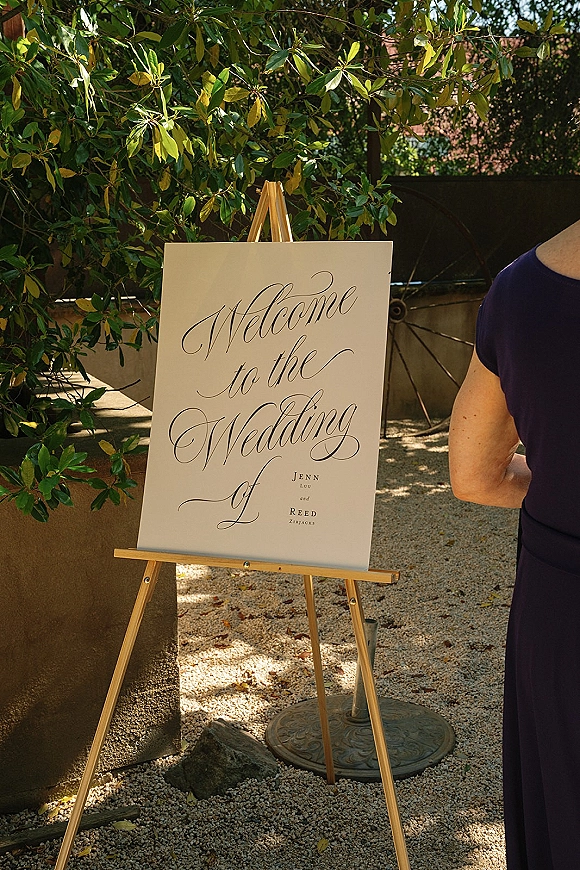 Wedding welcome sign with calligraphy wedding welcome sign lettering on a wooden easel, printed names, set by green foliage and a wagon wheel