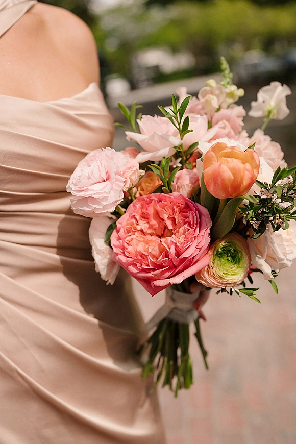 Bridal bouquet with a pink peony bouquet of peonies, ranunculus and sweet peas, ribbon wrapped, held against blurred garden greenery backdrop