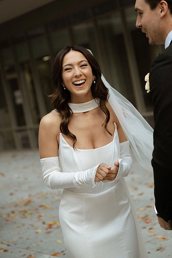 Bride portrait of a laughing bride in a strapless satin wedding dress and veil, holding hands with groom on an arched outdoor walkway