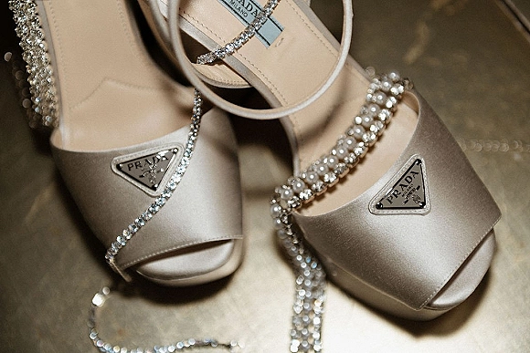 Bridal shoes in a wedding shoes close up showing rhinestone ankle straps and pearl embellishments with a Prada plaque on stone floor