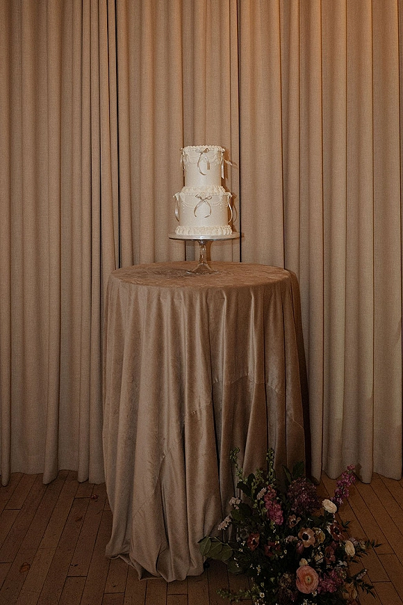Wedding cake with two tier wedding cake design, ribbon bows and piped frosting on a stand with florals before draped curtains