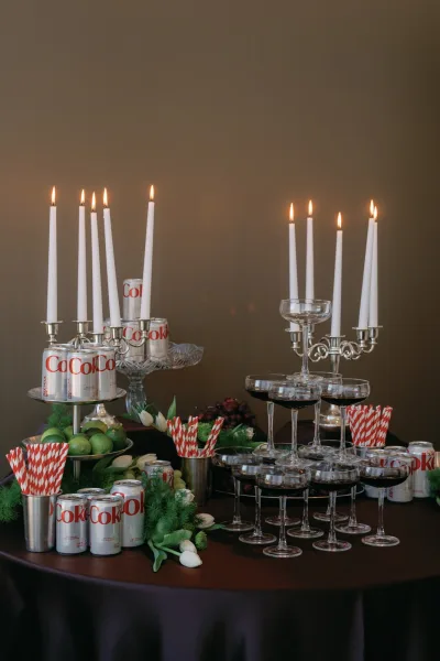 Wedding drink station with a wedding bar setup of coupe glasses, soda cans, limes, tulips, and taper candles on a wooden table