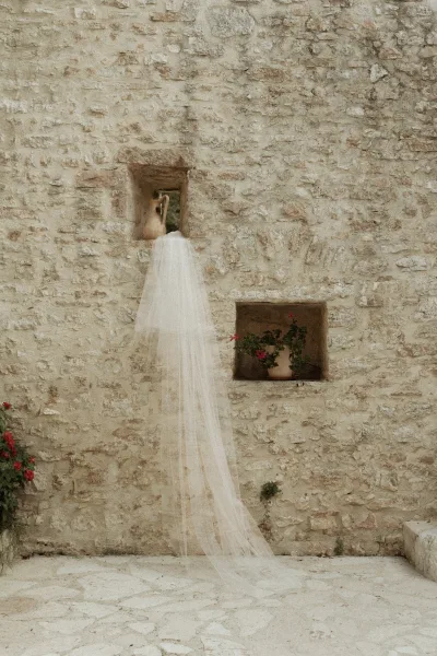 Bridal veil, cathedral length veil draped in long tulle against a rustic stone wall with niches, styled beside a ceramic jug and potted flowers