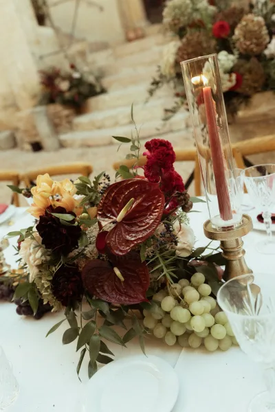 Reception tablescape with wedding table centerpiece of anthurium and hydrangea, grapes, and taper candles on an outdoor stone patio table
