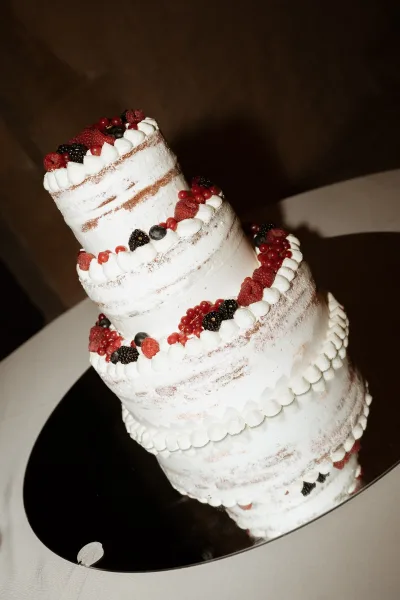 Wedding cake with tiered wedding cake design, textured buttercream and piped frosting, topped with fresh berries on a stand against dark backdrop