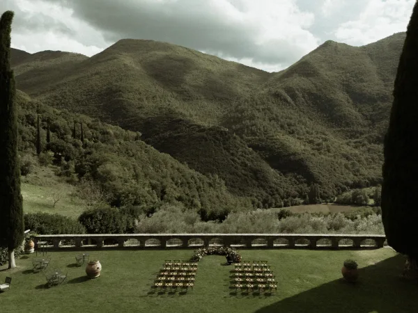 Ceremony setup for an outdoor wedding ceremony with chairs around ground florals on a stone terrace, overlooking mountains and valley under clouds