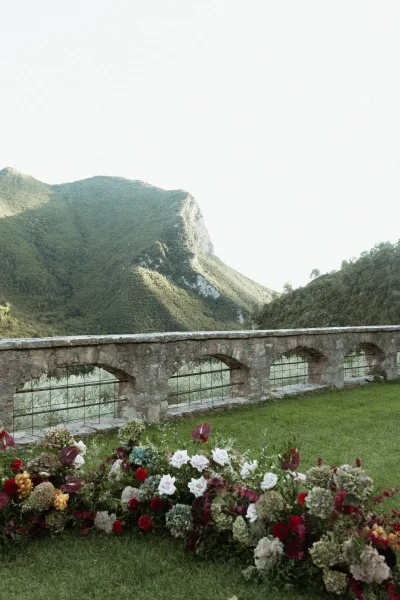 Ceremony floral arrangement of roses, hydrangeas, anthuriums and greenery spread along grass, framed by a mountain-view stone terrace