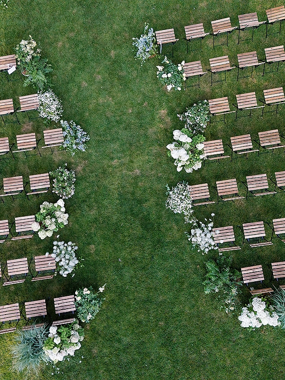 Ceremony aisle design with outdoor wedding aisle of wood folding chairs lining a grass lawn, accented by white and blue floral clusters and greenery