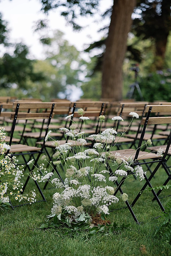 Ceremony seating with outdoor wedding ceremony chairs, wood folding rows on grass with white wildflower aisle markers in a garden setting