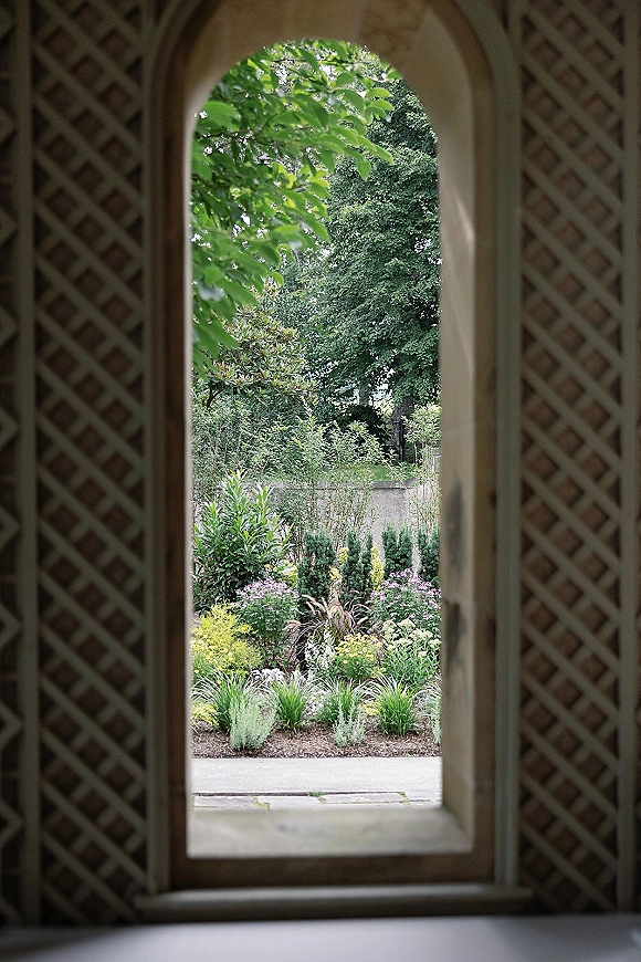 Garden view of a wedding venue garden framed by an arched doorway with lattice screen, looking onto a path, trees, and flower beds