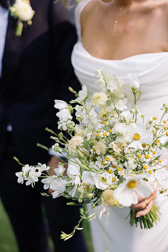 Bridal bouquet of white daisies and chamomile in a wildflower wedding bouquet, held by a bride in a strapless dress on a green lawn