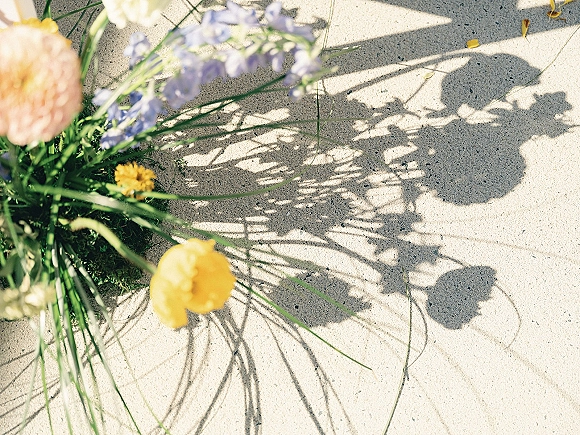 Wedding bouquet of wildflowers and greenery tied with a ribbon, resting on a sunlit concrete sidewalk with soft shadows