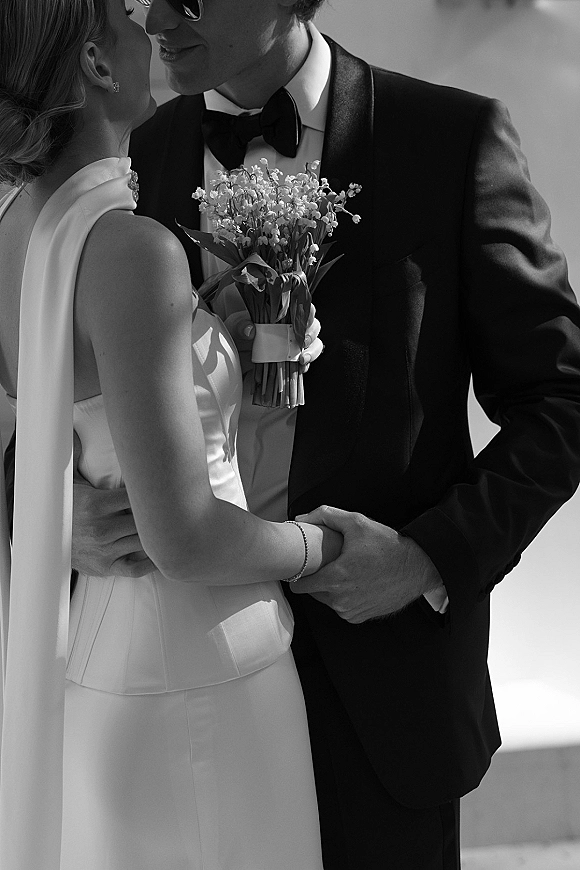 Wedding couple portrait in black and white, bride in strapless satin gown and veil embracing tuxedoed groom in sunglasses on an outdoor terrace