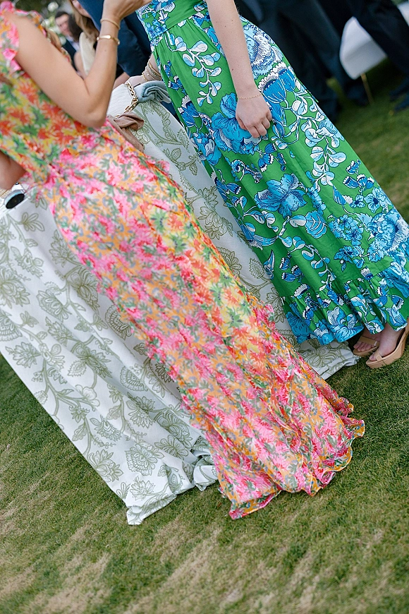 Wedding guest dresses in colorful floral maxi dress wedding styles with ruffled hems, clutch purse and nude sandals on a grass lawn