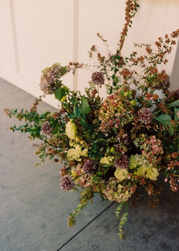 Wedding floral arrangement ground floral arrangement with hydrangeas, greenery and branches on a concrete floor beside a white door