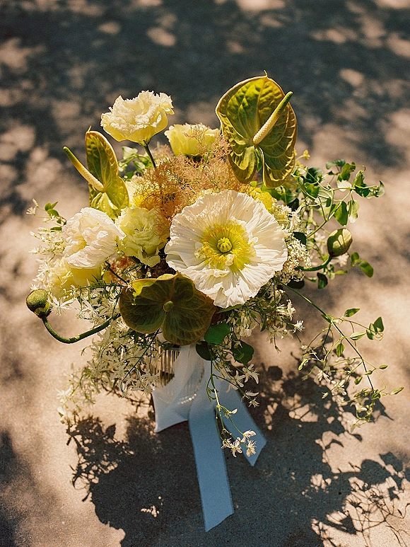 Wedding bouquet with white and green blooms and green anthurium, tied with a white ribbon, resting on sun-dappled concrete pavement