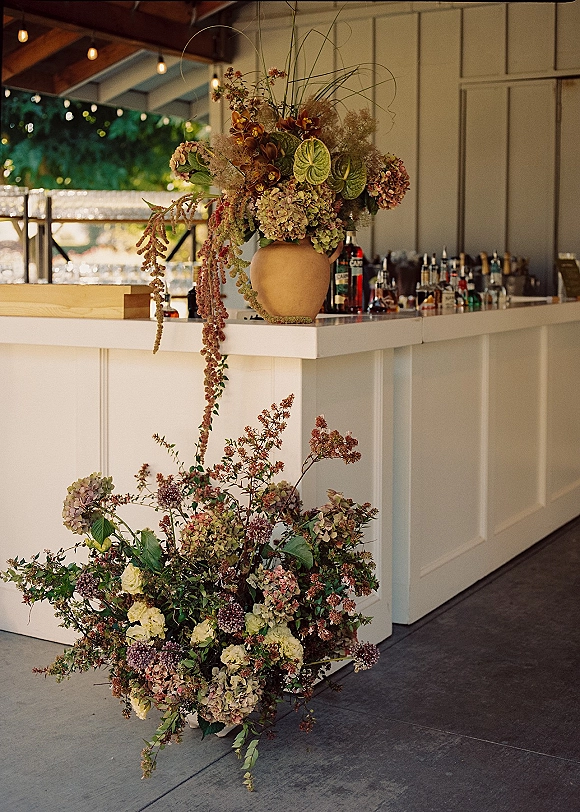 Wedding bar decor with a wedding bar floral arrangement in a terracotta vase, cascading greenery and string lights on a white paneled bar