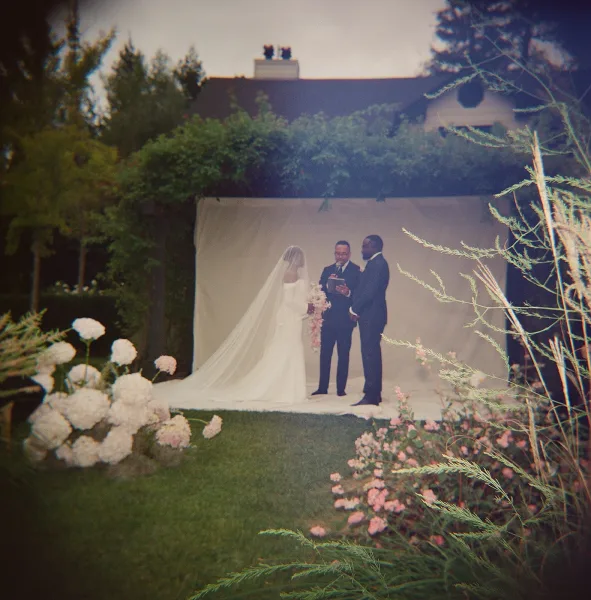 Ceremony moment at an outdoor wedding ceremony as bride in long veil and groom in suit stand with officiant before draped backdrop on lawn