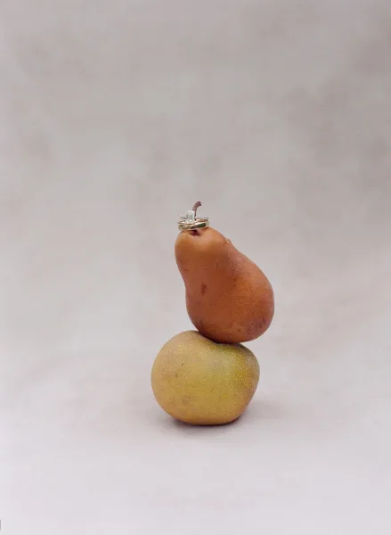 Wedding rings with engagement ring detail stacked on ripe pears against a neutral backdrop, highlighting a solitaire diamond and gold band