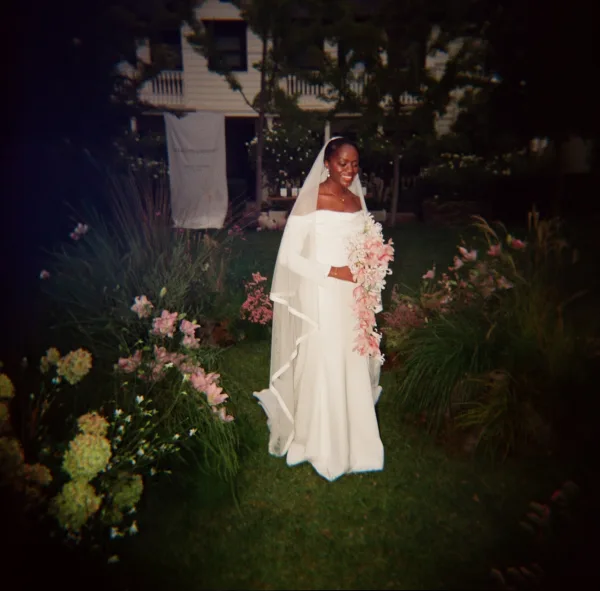 Bridal portrait of a bride holding bouquet in an off the shoulder wedding dress with cathedral veil on a garden lawn by a house porch railing
