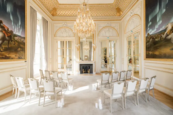Indoor ceremony setup featuring ballroom ceremony decor and a glowing fireplace, in a gilded ballroom with paneled walls and large windows.