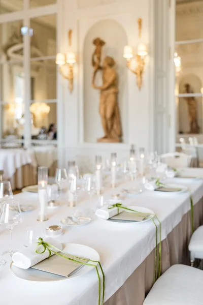 Reception tablescape on a modern wedding table glowing with taper candles, framed by mirrored panels, wall sconces, and classical statues.