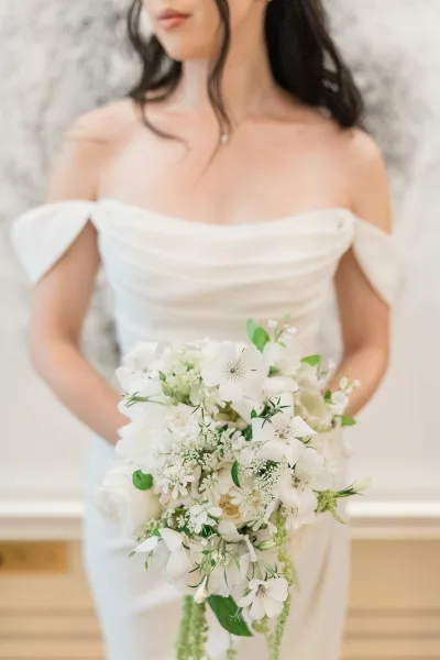 Bridal bouquet, a cascading white bridal bouquet with trailing greenery, cradled against an off-the-shoulder bridal gown.