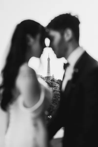 Couple portrait in a black and white wedding photo, groom in a bow tie as the couple shares a quiet moment beneath the Eiffel Tower and trees.