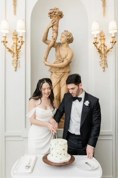 Wedding cake cutting with a couple holding a cake knife to slice a one-tier green and white buttercream floral cake