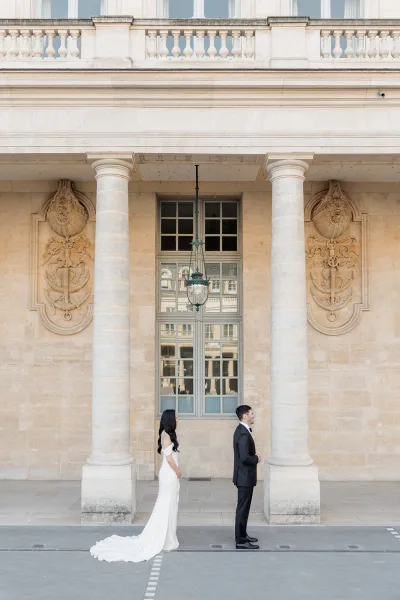 First look moment with the bride walking up to the groom, her gown train trailing, framed by stone columns and a carved facade with a hanging lantern.