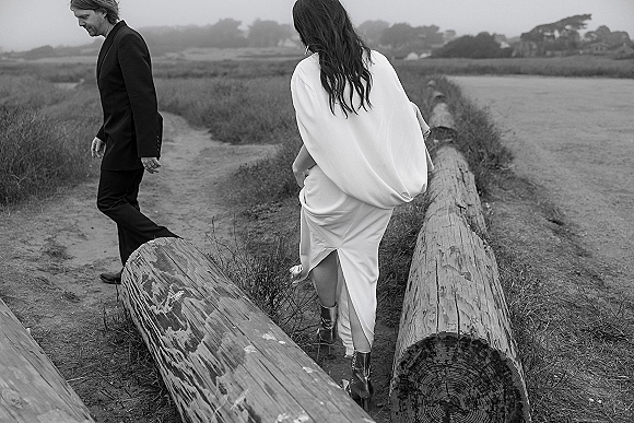 Couple portrait in a black and white wedding photo, bride in a white dress with ankle boots and groom in black suit on a coastal path by water