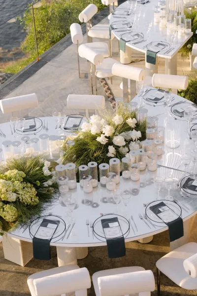 Reception tablescape showcasing outdoor reception decor with glowing candles on a waterfront stone patio framed by greenery.