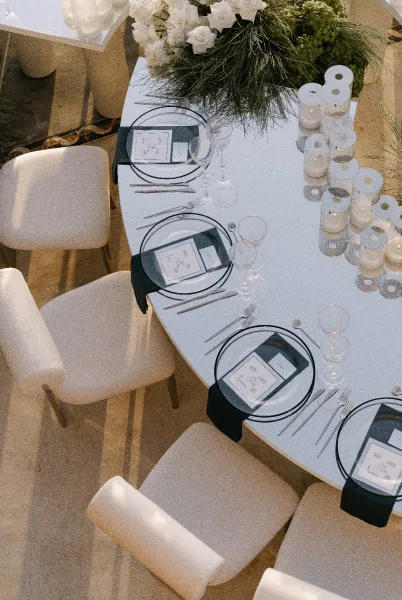 Reception tablescape for a mirrored tabletop wedding with a white rose centerpiece, as sunlight casts soft shadows across the stone floor.