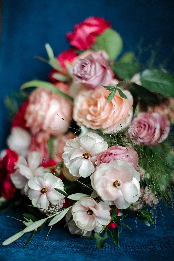 Wedding bouquet with colorful bridal bouquet roses and ranunculus, lush greenery accents, arranged on a blue fabric backdrop