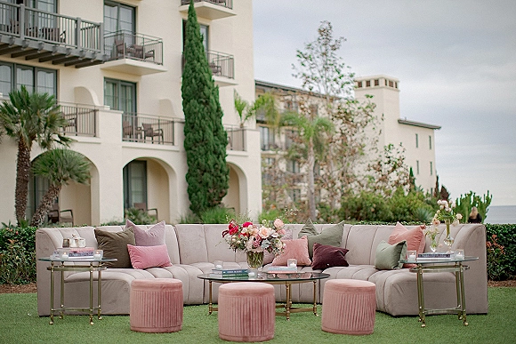 Lounge seating decor with a sectional sofa, throw pillows, and pink velvet ottomans around a glass coffee table on a resort lawn with palms