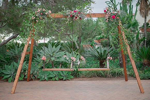 Wedding swing backdrop with floral swing backdrop garland of roses and greenery on a wooden A-frame bench swing in a lush garden setting