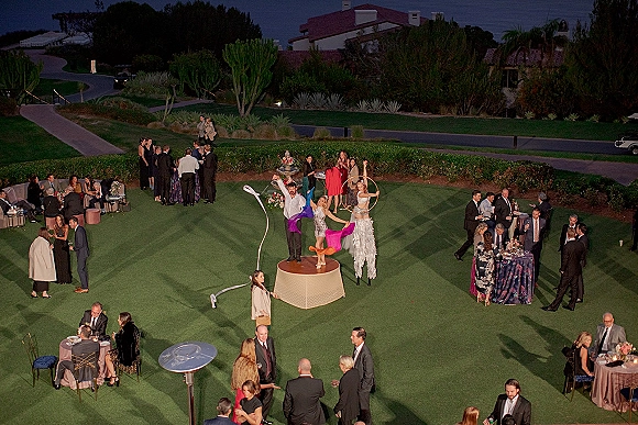 Wedding reception entertainment with wedding performers, a stilt walker and aerial ribbon dancer on a lawn patio with ocean view cocktail tables