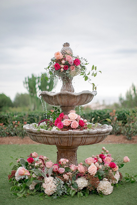 Floral fountain decor with wedding fountain flowers, pink and peach roses and white hydrangeas cascading around a stone tiered fountain on a lawn