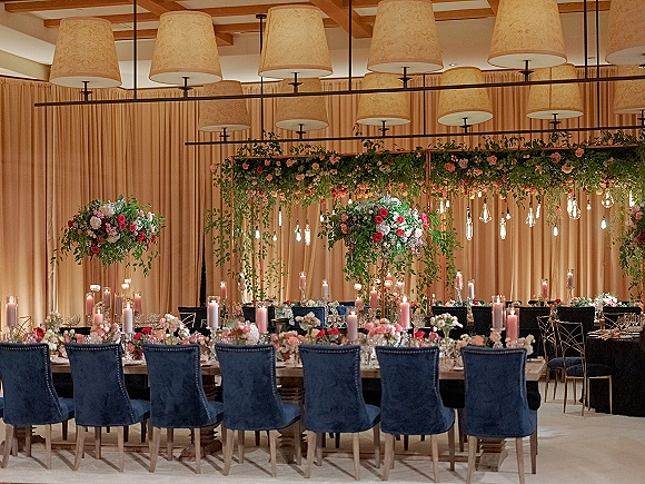 Reception tablescape with wedding head table decor, pink taper candles and lush florals beneath hanging greenery in a draped ballroom