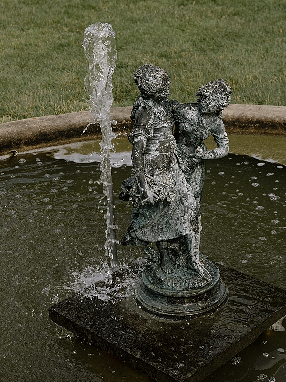 Garden fountain with a bronze statue spouting water into a circular basin, set on a grass lawn with stone edging