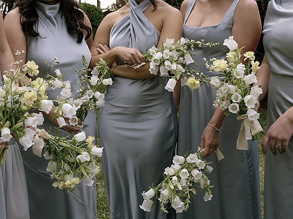 Bridesmaid dresses in blue satin with bouquets and ribbon wrap, showing mix-and-match necklines against lush garden greenery