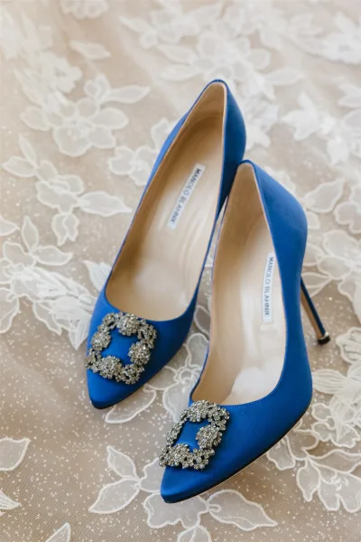Bridal shoes in blue wedding shoes style, satin pumps with crystal buckle and pointed toes resting on delicate lace fabric flatlay