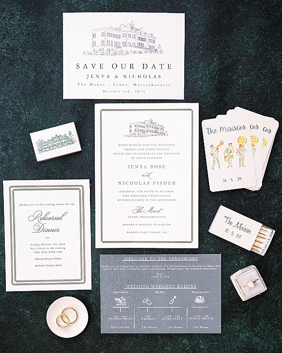 Wedding invitation suite with classic wedding invitations, save the date, itinerary cards, matchbook, and rings on dark textured fabric flatlay