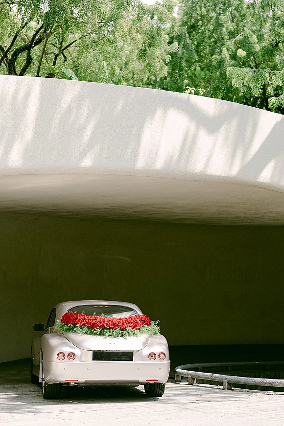 Wedding getaway car with wedding car decoration, red rose and greenery garland draped across the trunk near a tunnel underpass roadway