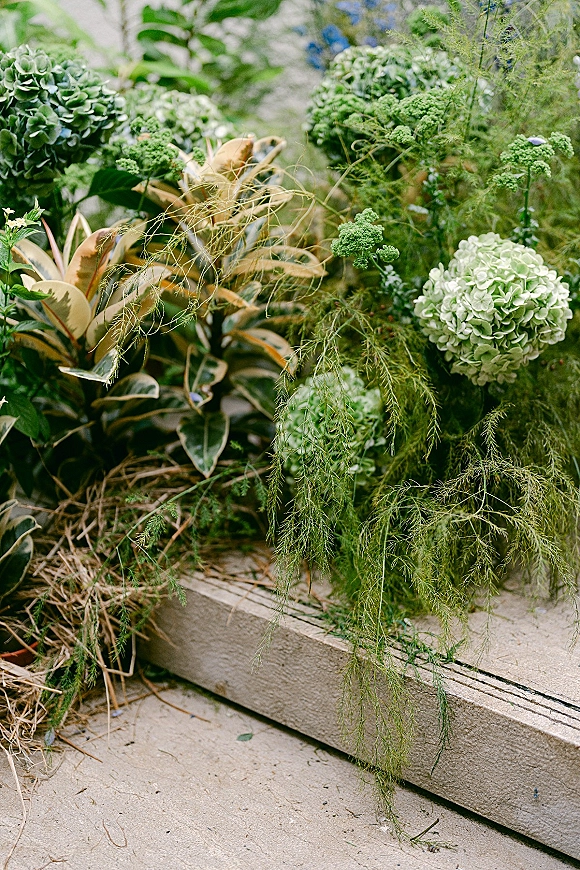 Wedding floral arrangement with green hydrangea and trailing greenery resting on stone steps beside garden plants for ceremony decor