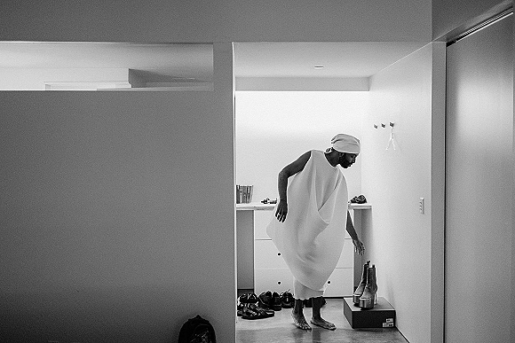 Getting ready moment as a bride in a bridal getting ready scene, adjusting her gown and head wrap beside a dresser in a minimalist room