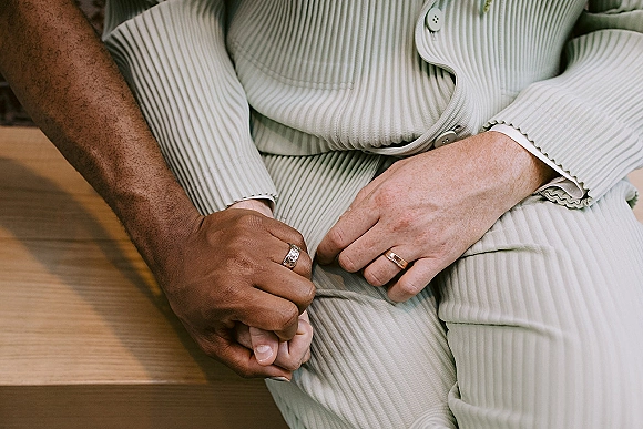Wedding rings on hands, wedding band close-up with textured bands beside light grey suit buttons on a wooden bench background